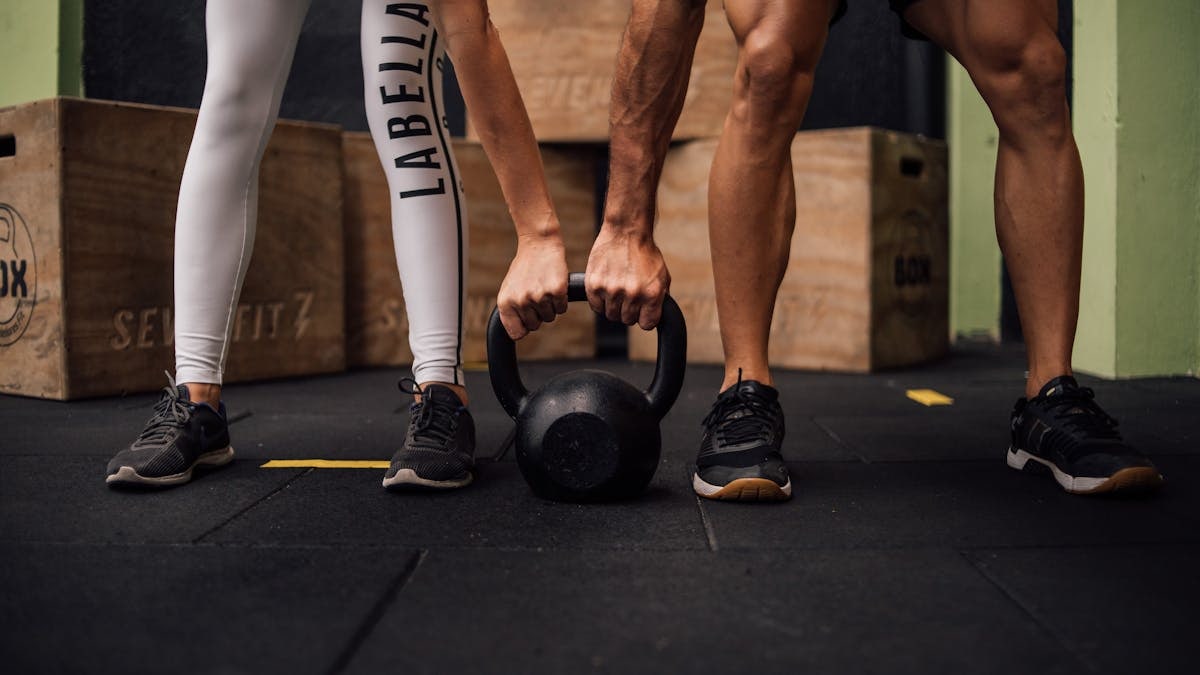 A man and woman engaging in CrossFit training with a kettlebell at an indoor gym in Brazil.